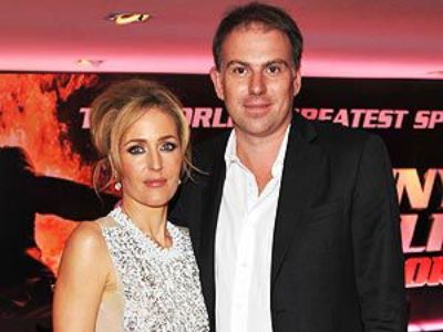 Gillian Anderson is wearing a sleeveless silver colored dress and Mark Griffiths is wearing a black suit with a white shirt.